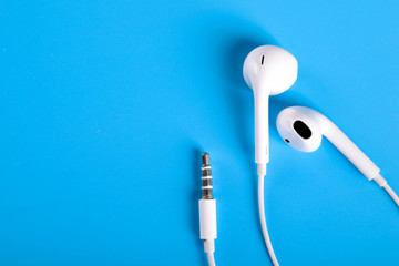 Mobile headphones of white color on a blue background in light colors with a place for text , copyspace. Top view.
