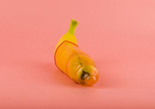 Banana in a condom on a pink background close-up