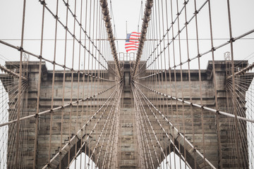 Details of the architecture of the famous Brooklyn Bridge with the American flag - New York City, NY