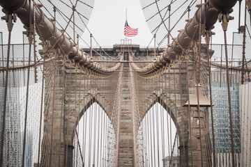 Fototapeta premium Details of the Brooklyn Bridge Architecture with the American Flag Floating at the Top of the Arch - New York City, NY