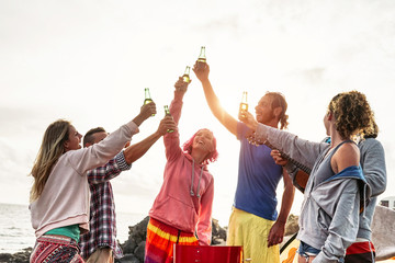 Group of friends making party and toasting with beers at sunset - Young happy people having fun at barbecue dinner outdoor - Millennial, summer, vacation and youth holidays lifestyle concept