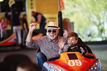 Foto auf Leinwand Großvater und Enkel haben Spaß und verbringen gute Zeit zusammen im Vergnügungspark. Sie genießen und lächeln, während sie zusammen Autoscooter fahren. © Dusko