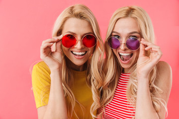 Happy blonde twins holding their sunglasses and looking at camera