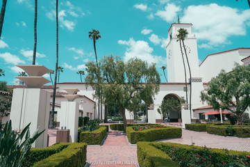 Union Station in Los Angeles California USA. beautiful summer spring weather outdoor in america. forecourt green garden park trees of historical building with tall clock tower showing time blue sky. - obrazy, fototapety, plakaty