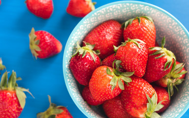 fresh bright strawberries in a bowl top view on a blue background