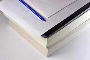 Stacked books and notebook with paper and pen on top
