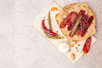 Basturma, dried tenderloin of beef meat, jerky, thinly sliced. Dry rosemary, pepper mix, chili, garlic on vintage linen cloth. Delicious food on a wooden board, stone background, copy space, top view.