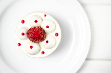 White airy cake with raspberry layer and raspberry berry lies on a white round plate next to a white cup, which stands on a white table