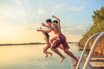 A group of young people joyfully jump into the refreshing lake waters on a sunny summer day, embracing the carefree moments of pure fun and laughter.