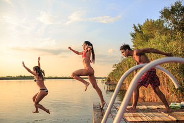 A group of young people joyfully jump into the refreshing lake waters on a sunny summer day,...