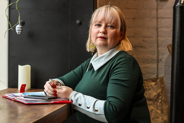 A thick blond woman works in a cafe. A business woman writes in a notebook. Work freelancer.