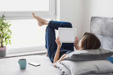Young beautiful woman resting at home using digital tablet computer. Happy girl reading or shopping online. Relaxation, leisure, freelance work concept