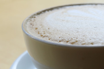 A cup of coffee with heart pattern in a white cup on wooden background