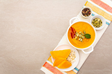 Pumpkin cream soup. White ceramic bowl with fresh pumpkin, dry seeds, smoked bacon. With vintage linen cloth (napkin) on stone background, top view