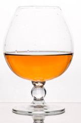brown alcohol drink in crystal glass on white background with reflection