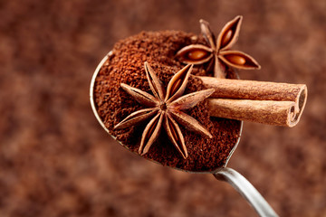 Spoon of ground coffee with anise and cinnamon on the background of coffee beans.