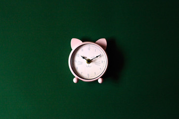 Pink alarm clock in the form of a cat on a green background.