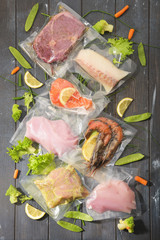 Sous Vide cooking concept. Vacuum packed ingredients arranged on wooden dyed background.