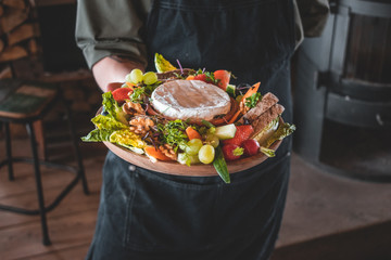 Delicious camembert fondue with fruit and bread to dip, strawberries, grapes, walnuts radishes with hold in hand by chef
