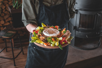Delicious camembert fondue with fruit and bread to dip, strawberries, grapes, walnuts radishes with hold in hand by chef