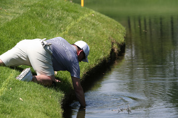 A golfer reaches into a pond to retrieve his ball