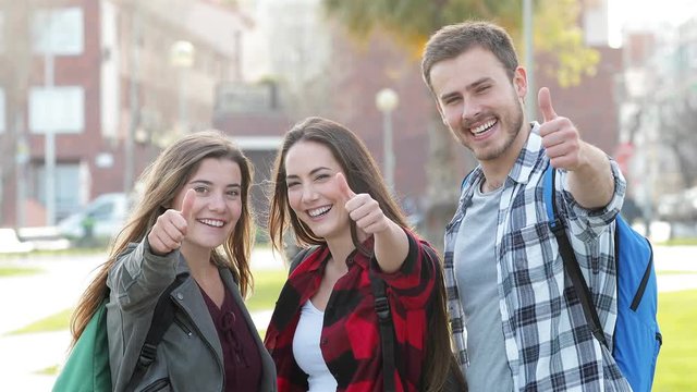 Front view of three students gesturing thumbs up at camera in the street