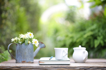White cup and white pot and flowers in rustic watering pot on wooden table