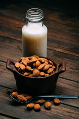 Wooden table with Almond milk and several almonds in a bowl