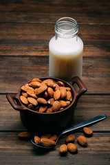 Wooden table with Almond milk and several almonds in a bowl