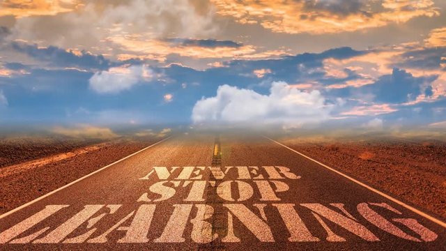 Landscape with text 'Never Stop Learning' written on the road, which leads to the horizon above which is a time lapse sky.