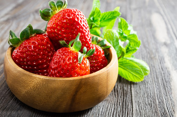 Fresh strawberries in wooden bowl and mint leaves on wooden background.