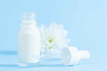 Natural cosmetics: serum with dropper and white flower on blue background.