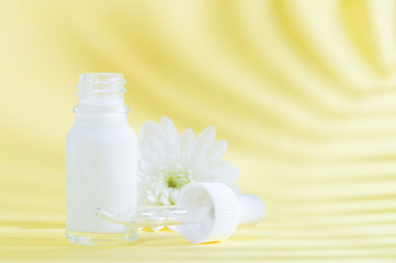 Fototapeta na wymiar Natural cosmetics: serum with dropper and white flower on yellow background with shadow.