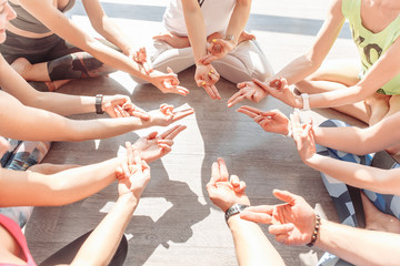 Group of young people doing mudra sit in a lotus position in a circle In the bright gym during meditation. Group yoga concept