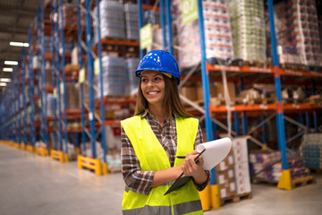 Portrait of female worker in distribution warehouse looking aside. Smiling woman with hardhat...