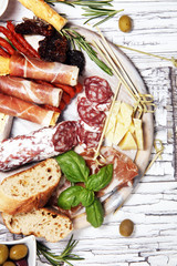 antipasto various appetizer. Cutting board with prosciutto, salami, cheese, bread and olives on white wooden background