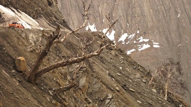 Close-up low-angle still shot of a glacier filled section of Zoji La, Ladakh highest mountain pass. Vehicles are slowly navigating their way through. At the valley side is a steep bare slope with
