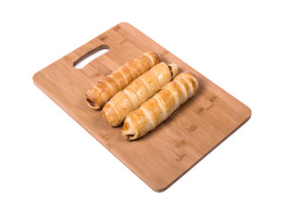 three sausages in dough on a wooden board, background is white