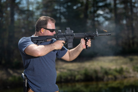 A man aiming an assault rifle with the empty shell in the air.