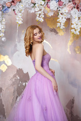 Elegant bride in a long lush lilac dress with a train under the arch of flowers.
