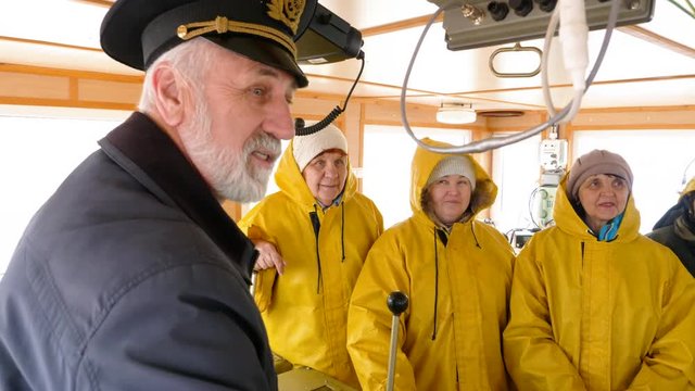 Bearded captain speaking with ship team in yellow uniform in navigation office. Female ship crew and captain meeting in navigation bridge. Sailing and shipping concept