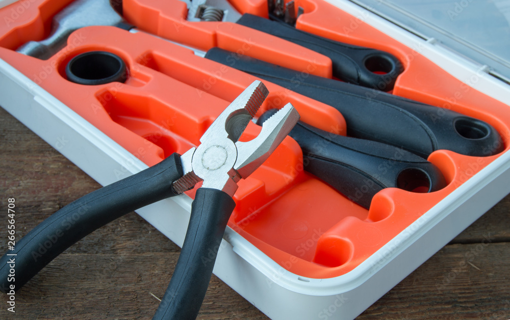 Wall mural Tool kit pliers, hammer, screwdriver in orange plastic case on old wooden Board with copyspace