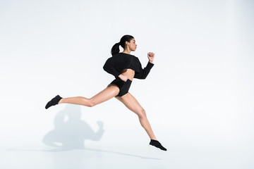 Fototapeta na wymiar side view of sportive african american girl in black sportswear and sneakers running on white
