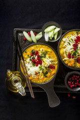 laks with pumpkin and coconut milk, rice noodles, broccoli and pomegranate seeds in portioned black plates onlaksa with pumpkin and coconut milk, rice noodles, broccoli and pomegranate seeds 