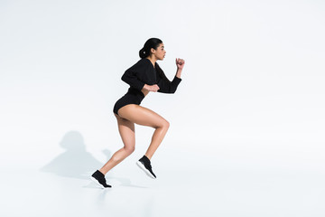 side view of beautiful sportive african american girl in black sportswear running on white