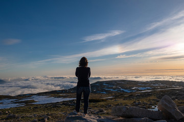 Amazing sunset view above clouds, with Young Woman Contemplating it, from Torre (Tower) The Highest Point in Portugal, Serra da Estrela, Portugal