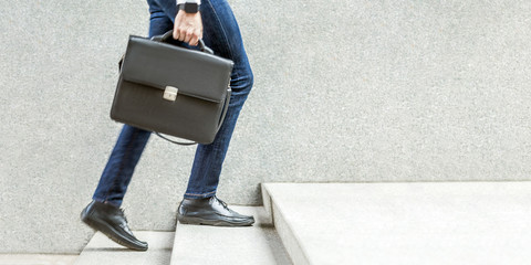 Businessman with black briefcase in hand walking up on stairs. - obrazy, fototapety, plakaty
