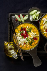 laks with pumpkin and coconut milk, rice noodles, broccoli and pomegranate seeds in portioned black plates onlaksa with pumpkin and coconut milk, rice noodles, broccoli and pomegranate seeds 