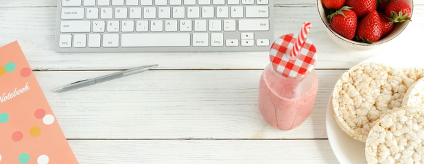 Healthy working life style banner . Laptop, notebook, cup of coffee, strawberries smoothie  and rice waffles on white wooden table. Top view, flat lay