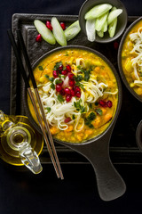 laks with pumpkin and coconut milk, rice noodles, broccoli and pomegranate seeds in portioned black plates onlaksa with pumpkin and coconut milk, rice noodles, broccoli and pomegranate seeds 